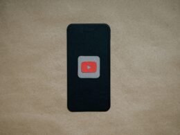 Schwarzes Smartphone mit prominentem roten YouTube-Logo auf dem Display, auf dunklem Hintergrund liegend