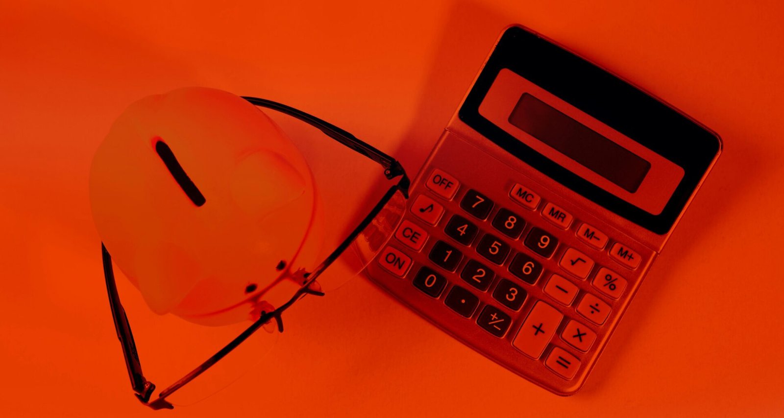 Ein rosa Sparschwein steht neben einem schwarzen Taschenrechner auf einem orangefarbenen Hintergrund.