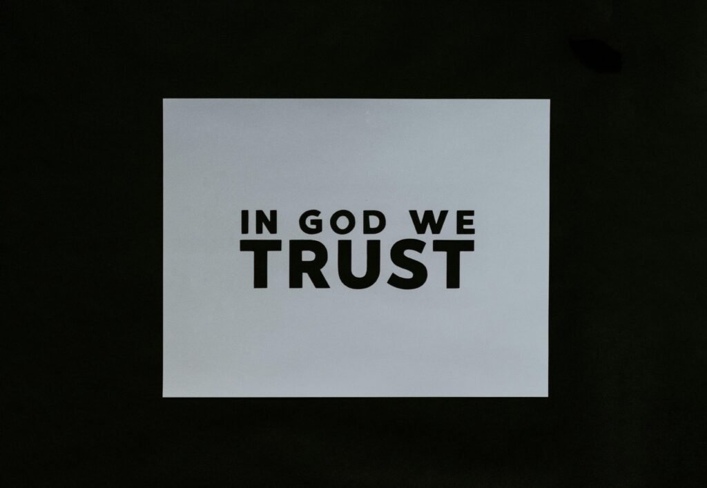 Ein Blatt Papier mit der Aufschrift 'In God We Trust' in klarer Schrift auf einer glatten Oberfläche platziert.