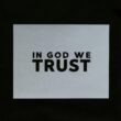 Ein Blatt Papier mit der Aufschrift 'In God We Trust' in klarer Schrift auf einer glatten Oberfläche platziert.