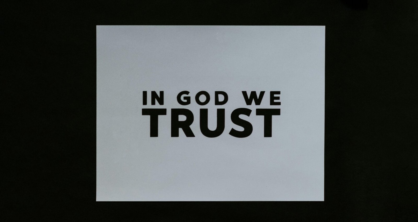 Ein Blatt Papier mit der Aufschrift 'In God We Trust' in klarer Schrift auf einer glatten Oberfläche platziert.