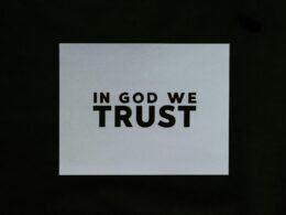 Ein Blatt Papier mit der Aufschrift 'In God We Trust' in klarer Schrift auf einer glatten Oberfläche platziert.