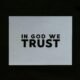 Ein Blatt Papier mit der Aufschrift 'In God We Trust' in klarer Schrift auf einer glatten Oberfläche platziert.
