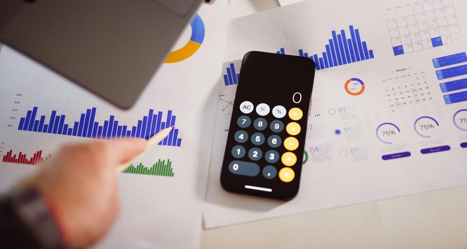 Taschenrechner auf einem Holztisch neben einem aufgeklappten Laptop, Fokus auf Arbeitsorganisation