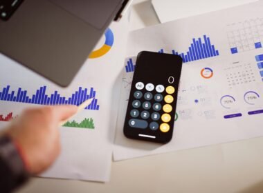 Taschenrechner auf einem Holztisch neben einem aufgeklappten Laptop, Fokus auf Arbeitsorganisation