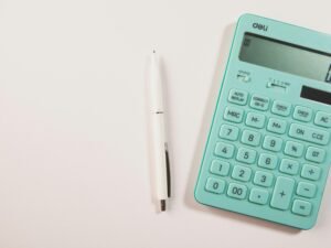 Ein türkisfarbener Taschenrechner neben einem weißen Stift auf weißem Hintergrund, geeignet für Themen wie Finanzen oder Online-Tools.