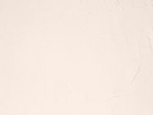 Eine schwarze Katze sitzt auf einem weißen Laken, fotografiert aus der Vogelperspektive, klarer Kontrast zwischen Katze und Untergrund.