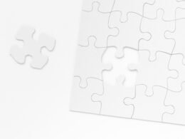 Ein weißes Puzzlestück liegt auf einer glatten Tischoberfläche, einzeln positioniert und voneinander getrennt.