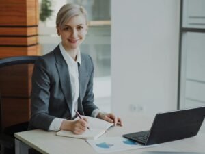 Eine Frau im Business-Anzug sitzt an einem Schreibtisch und arbeitet konzentriert an ihren Unterlagen im Büro.