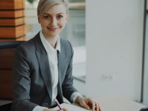 Eine Frau im Business-Anzug sitzt an einem modernen Schreibtisch in einem Büro und arbeitet konzentriert am Laptop.