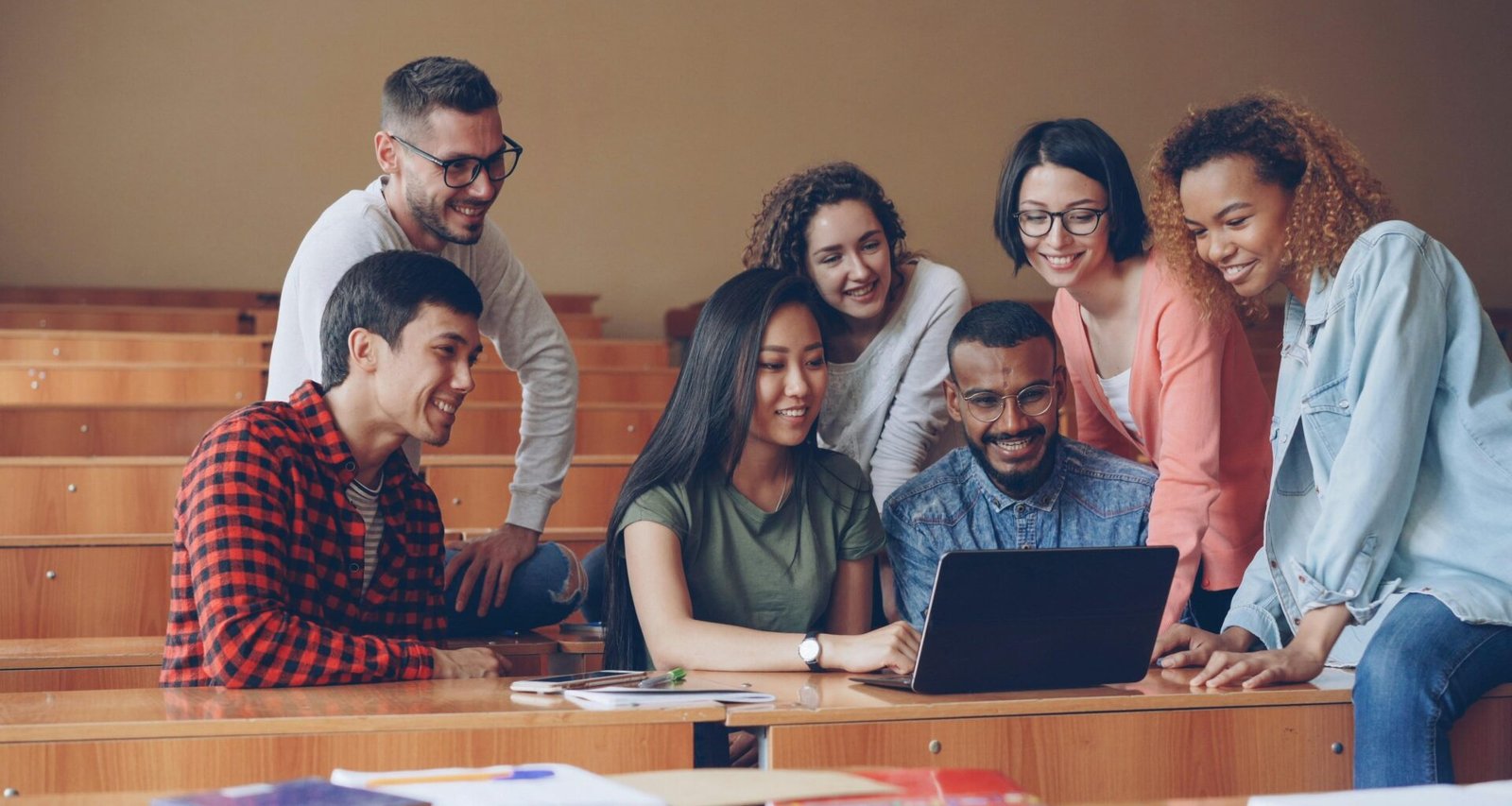 Eine diverse Gruppe Studierender sitzt zusammen um einen Laptop und arbeitet kollaborativ an einer Aufgabe