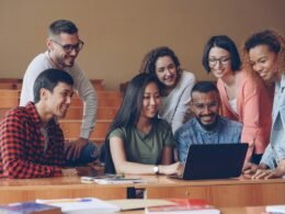 Eine diverse Gruppe Studierender sitzt zusammen um einen Laptop und arbeitet kollaborativ an einer Aufgabe