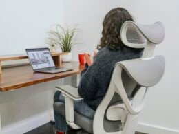 Frau sitzt an einem Schreibtisch und arbeitet an einem Laptop in einem modernen Büro mit dezentem Hintergrund.
