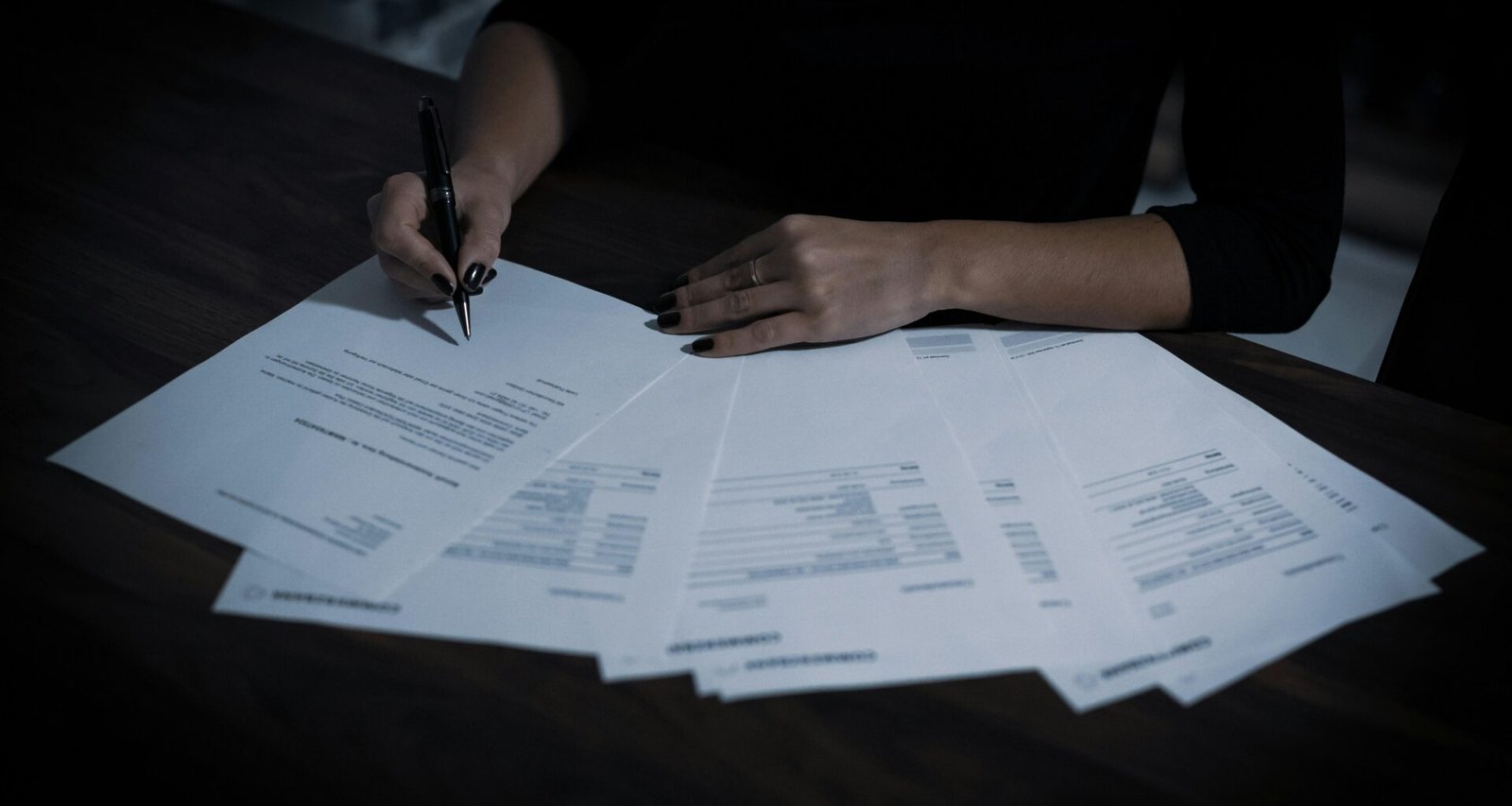 Frau sitzt an einem Tisch mit zahlreichen Papieren und arbeitet an Dokumenten, Schreibtisch voll Unterlagen