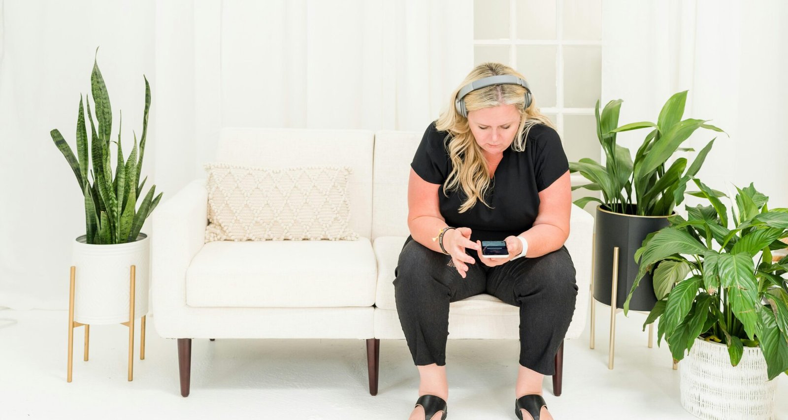 Eine Frau sitzt allein auf einem modernen Sofa im Wohnzimmer und blickt nachdenklich in die Ferne.