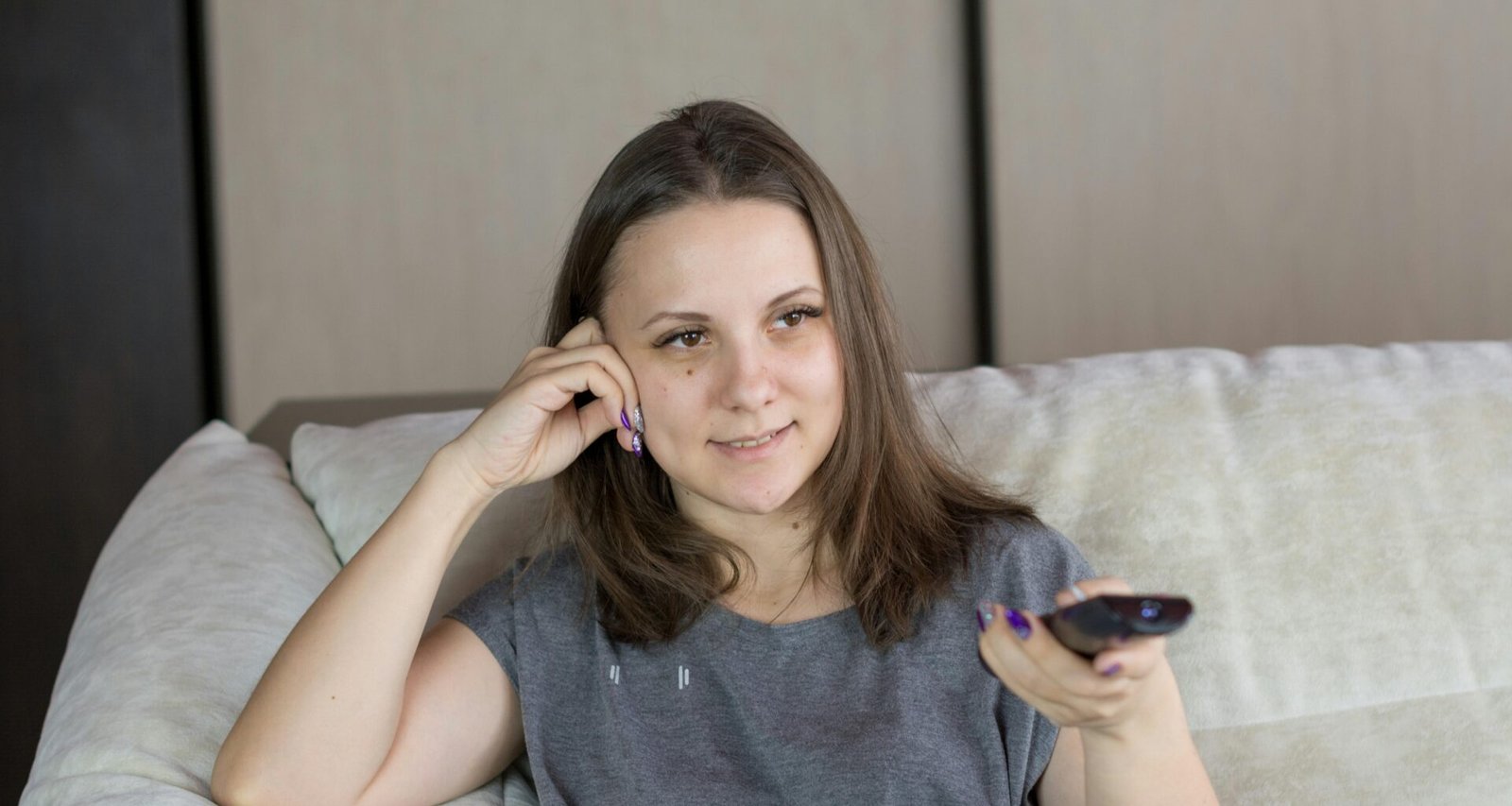 Frau sitzt auf einem Sofa und hält eine Fernbedienung, gemütliche Alltagsatmosphäre im Wohnzimmer