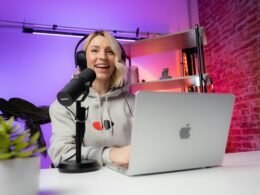 Eine Frau sitzt an einem Tisch vor einem Laptop und arbeitet in einem modernen Raum mit schlichter Einrichtung