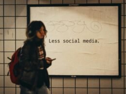 Frau steht vor einem Schild mit der Aufschrift 'Less Social Media', das zur Reflexion über digitalen Medienkonsum anregt.