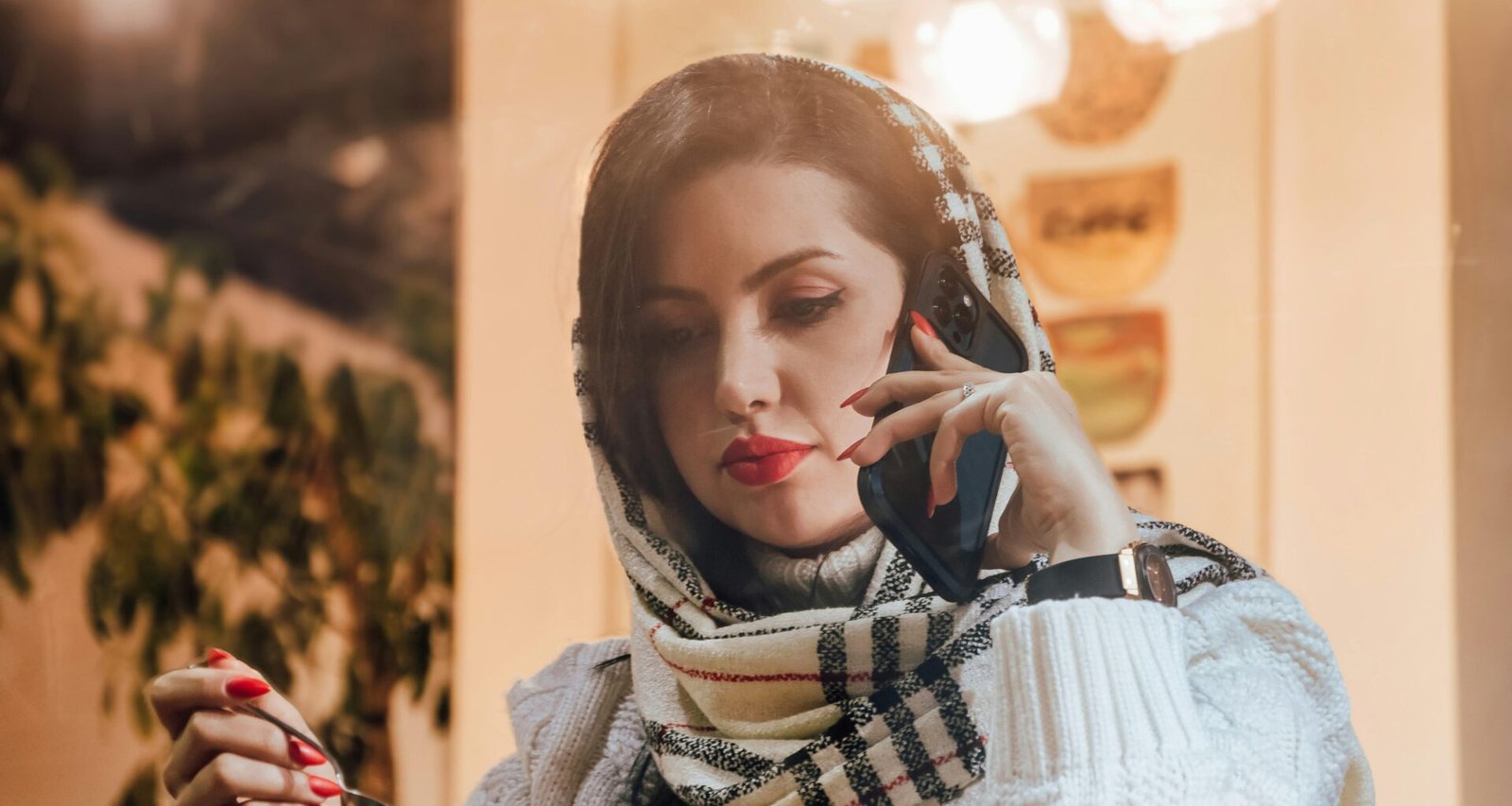 Frau hält eine Tasse Kaffee und spricht dabei unterwegs in ein Mobiltelefon, dargestellt in Alltagsszenerie