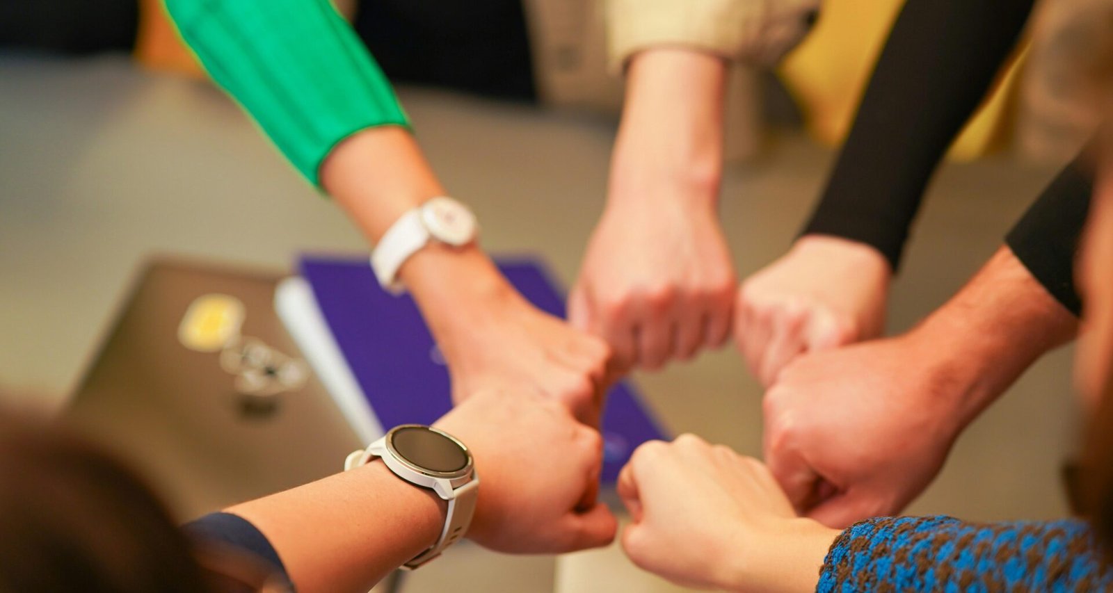 Mehrere Personen legen ihre Hände in der Mitte übereinander als Zeichen für Teamarbeit und Zusammenarbeit.