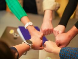 Mehrere Personen legen ihre Hände in der Mitte übereinander als Zeichen für Teamarbeit und Zusammenarbeit.