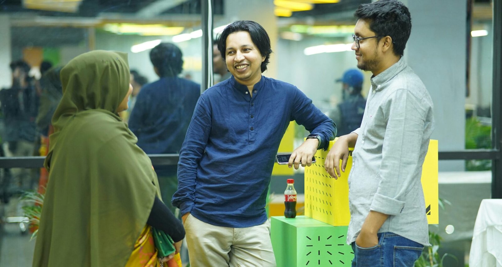 Mehrere Personen stehen um einen grünen Tisch in einem modernen Büro und arbeiten gemeinsam an einem Projekt.