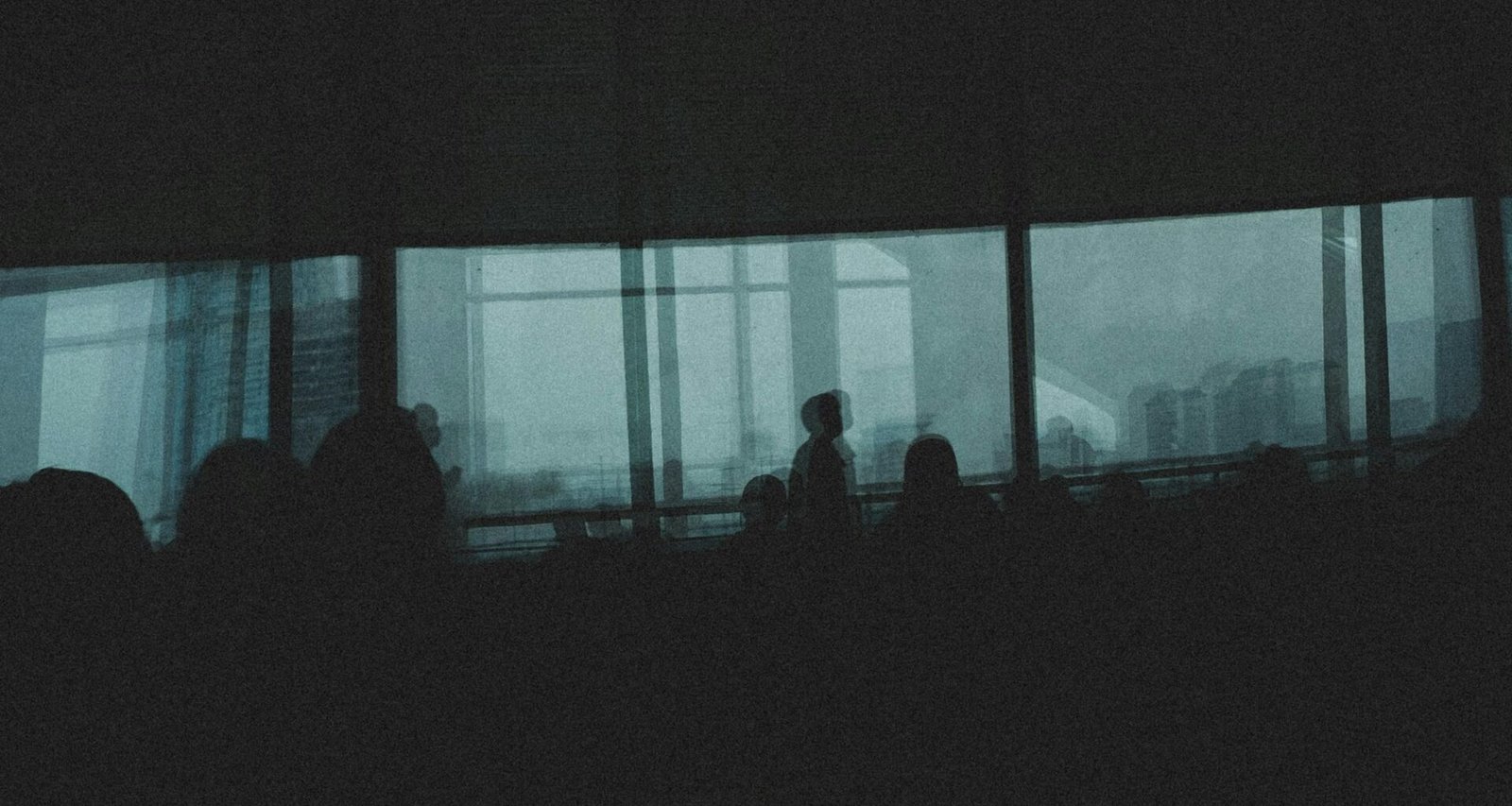 Eine Gruppe von Personen steht gemeinsam vor einem großen Fenster im Büro, die Silhouetten zeigen Teamarbeit.