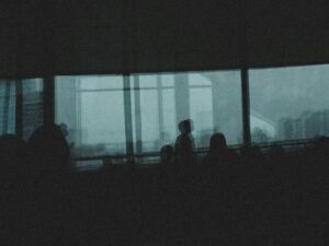 Eine Gruppe von Personen steht gemeinsam vor einem großen Fenster im Büro, die Silhouetten zeigen Teamarbeit.