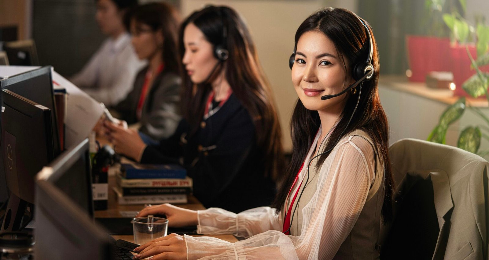 Frau mit Headset sitzt am Computerarbeitsplatz und unterstützt Kunden online per Chat oder Telefon.