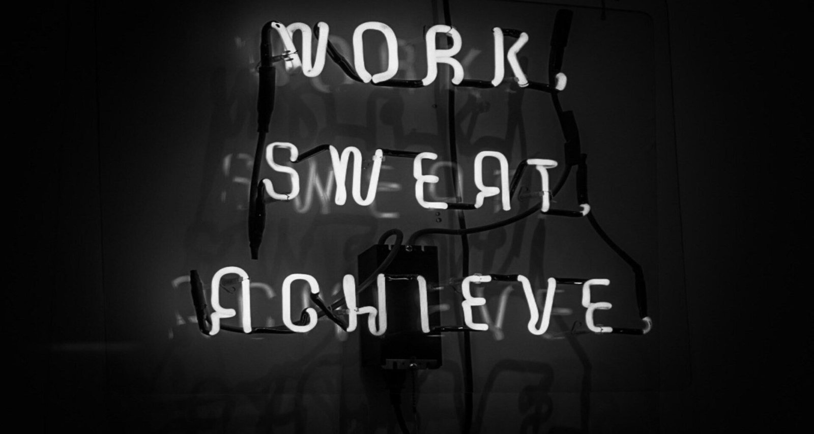 Leuchtendes Neon-Schild mit der Aufschrift Work, Sweat, Achieve vor dunklem Hintergrund