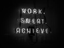 Leuchtendes Neon-Schild mit der Aufschrift Work, Sweat, Achieve vor dunklem Hintergrund