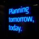 Leuchtendes Neon-Schild mit dem Schriftzug 'Planning tomorrow, today' vor dunklem Hintergrund
