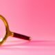 Eine Lupe liegt mittig auf einem gleichmäßig rosa Hintergrund, ideal für Artikel über Analyse und Suchmethoden.