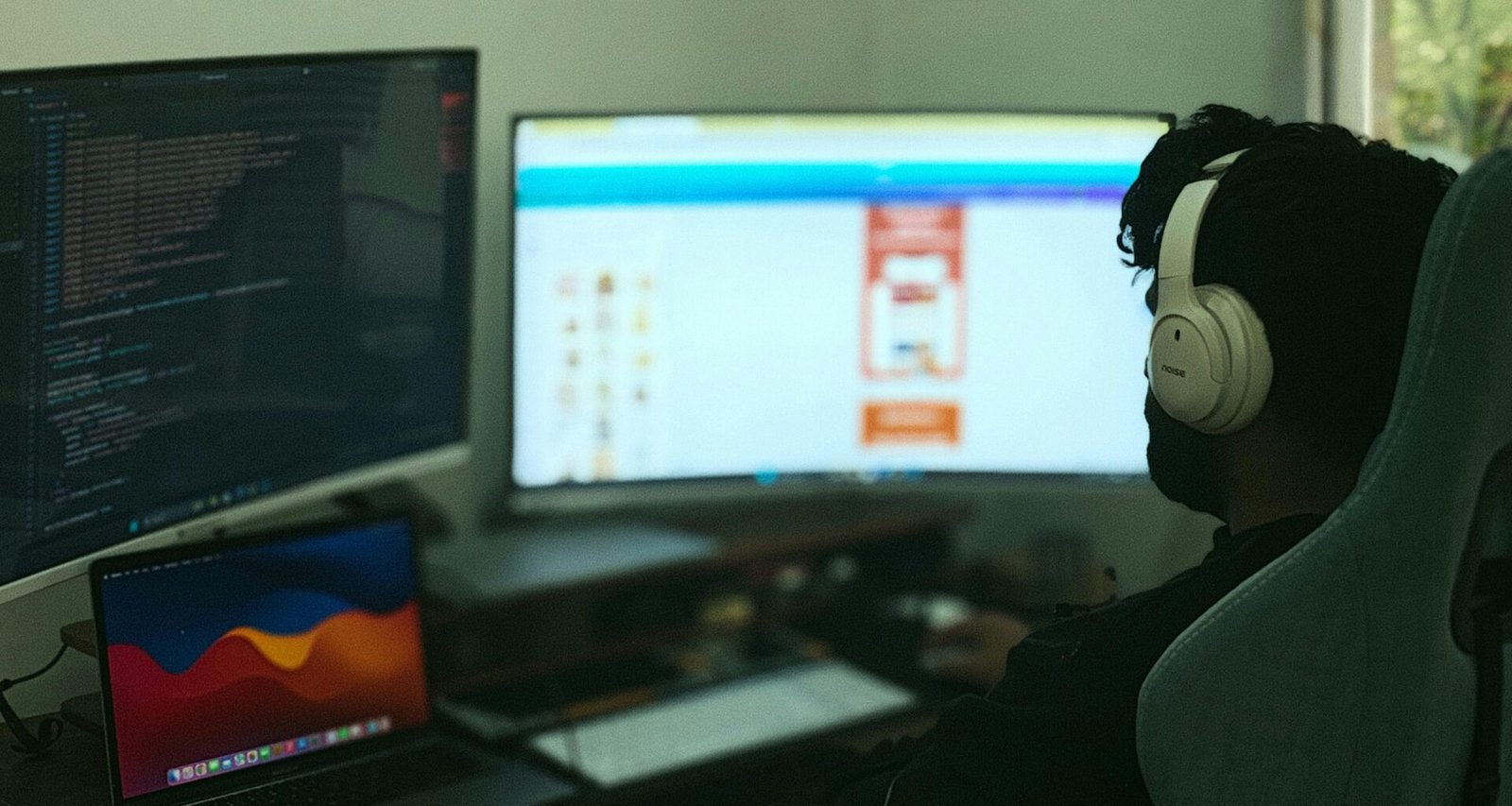 Person arbeitet an einem Schreibtisch mit mehreren Monitoren und Computer, umgeben von Technik im modernen Büro.