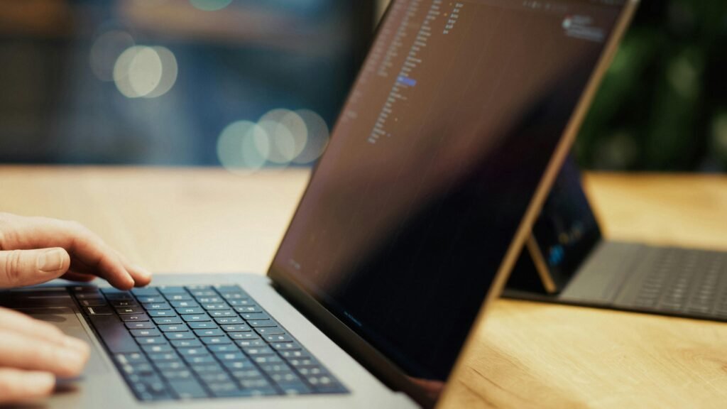 Eine Person tippt auf einem Laptop, der auf einem Holztisch steht – Fokus auf produktives Arbeiten mit digitalen Tools.