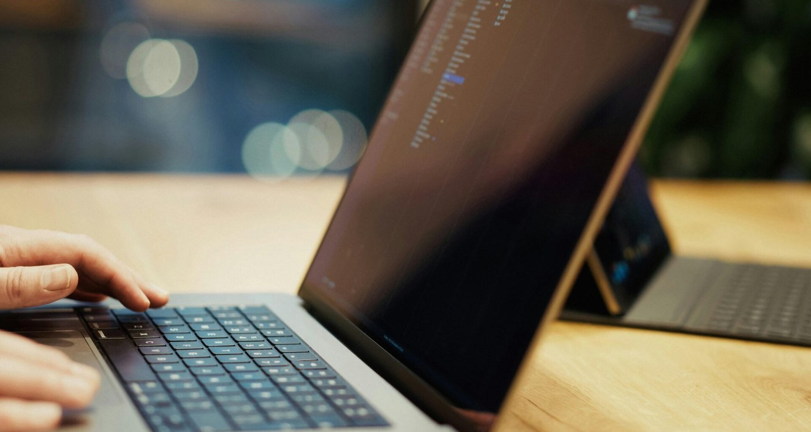 Eine Person tippt auf einem Laptop, der auf einem Holztisch steht – Fokus auf produktives Arbeiten mit digitalen Tools.