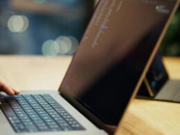 Eine Person tippt auf einem Laptop, der auf einem Holztisch steht – Fokus auf produktives Arbeiten mit digitalen Tools.