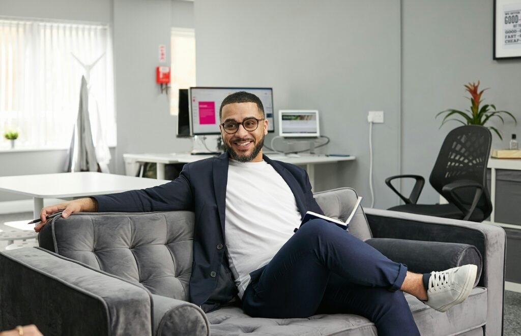Eine Person sitzt auf einer modernen Couch in einem Wohnraum. Das Bild vermittelt eine entspannte Arbeitsatmosphäre.