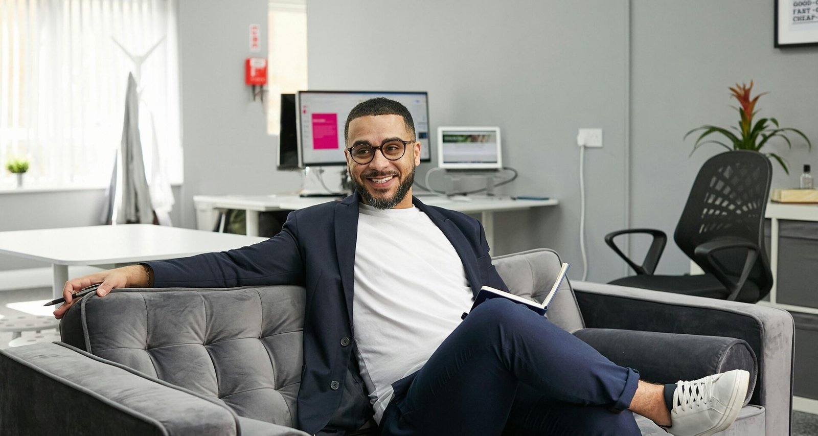 Eine Person sitzt auf einer modernen Couch in einem Wohnraum. Das Bild vermittelt eine entspannte Arbeitsatmosphäre.