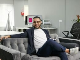 Eine Person sitzt auf einer modernen Couch in einem Wohnraum. Das Bild vermittelt eine entspannte Arbeitsatmosphäre.