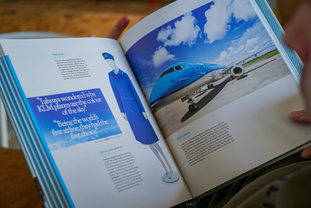 Eine Person hält ein geöffnetes Buch, auf dessen Seite ein Foto eines Flugzeugs zu sehen ist, Fokus auf Reisen und Technik