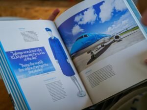 Eine Person hält ein geöffnetes Buch, auf dessen Seite ein Foto eines Flugzeugs zu sehen ist, Fokus auf Reisen und Technik