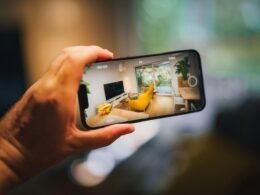Eine Person fotografiert ein helles, modern eingerichtetes Wohnzimmer mit Smartphone oder Kamera aus der Perspektive hinter dem Fotografen