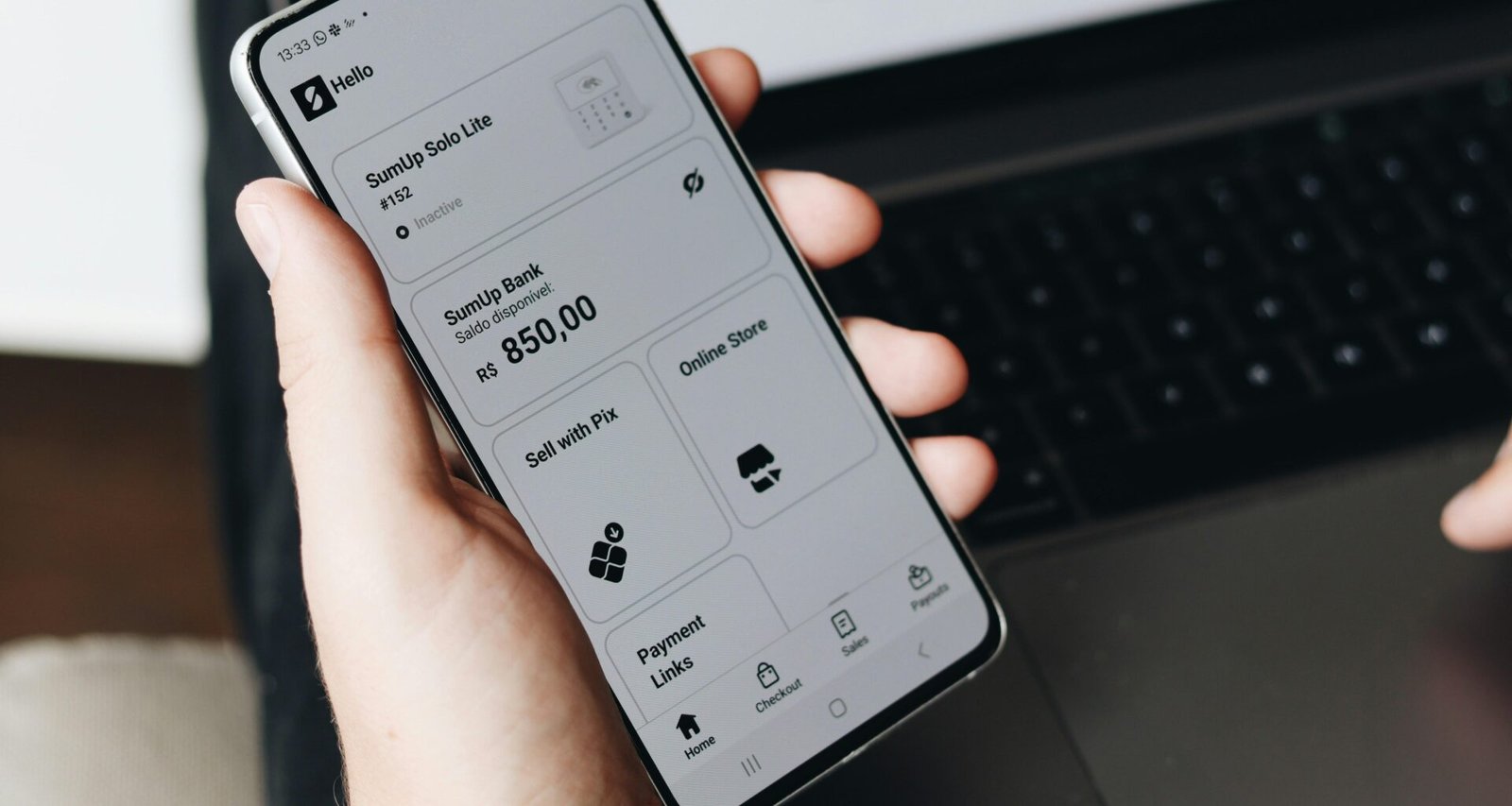 Eine Person hält ein Smartphone in der Hand und sitzt vor einem aufgeklappten Laptop, beide Geräte werden gleichzeitig verwendet.