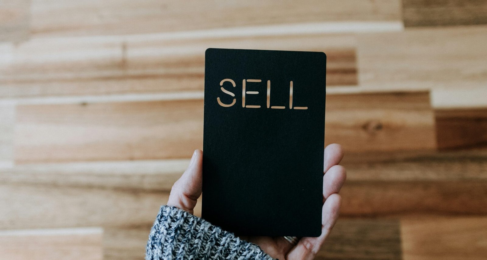 Person hält ein schwarzes Buch mit der Aufschrift 'Sell' in der Hand, geeignet für Artikel über Online-Vertrieb oder Verkaufsstrategien.