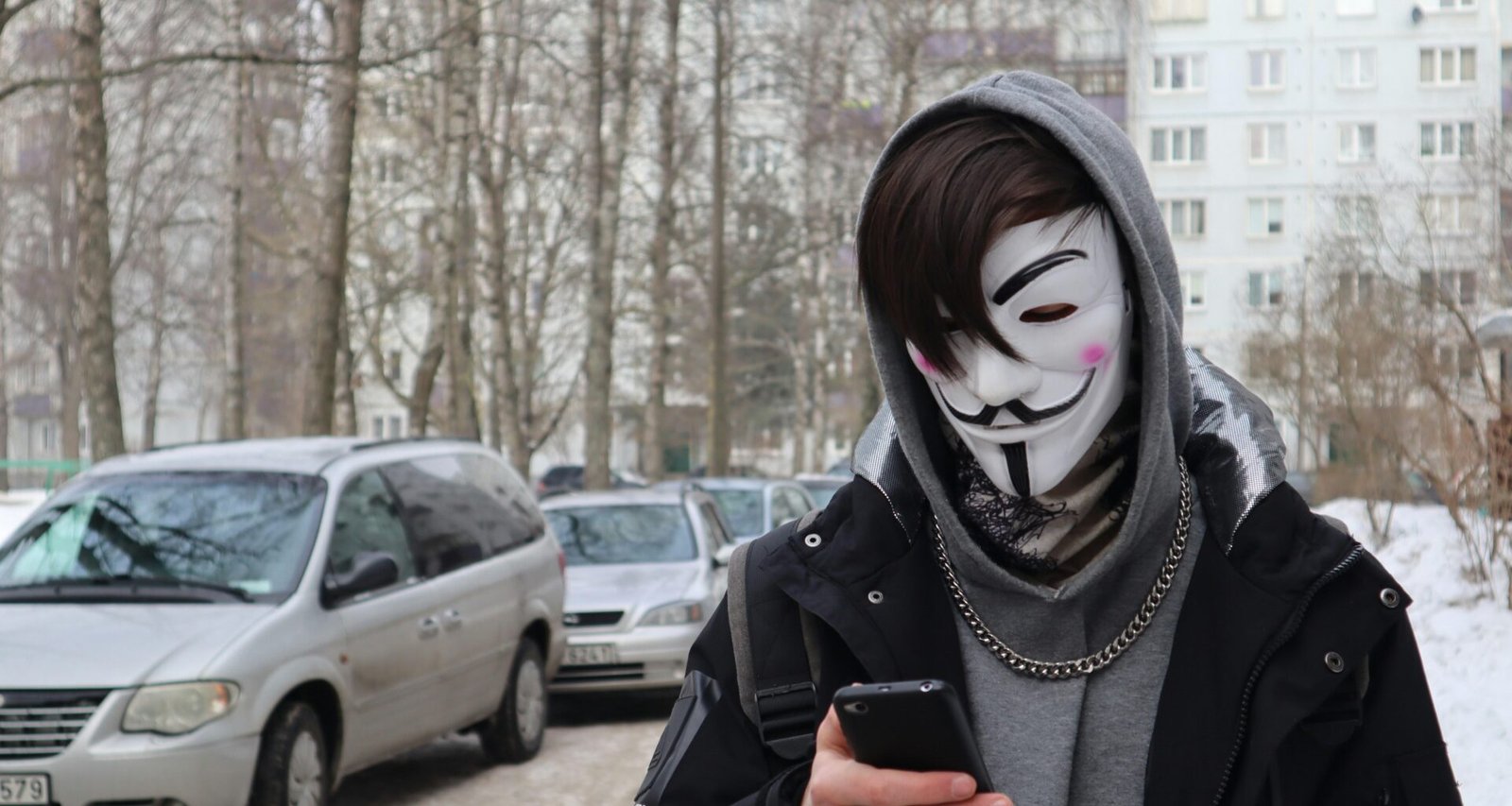 Eine Person mit Maske hält ein Smartphone in der Hand, Fokus auf die digitale Kommunikation im öffentlichen Raum.