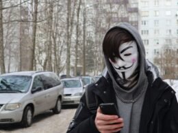 Eine Person mit Maske hält ein Smartphone in der Hand, Fokus auf die digitale Kommunikation im öffentlichen Raum.