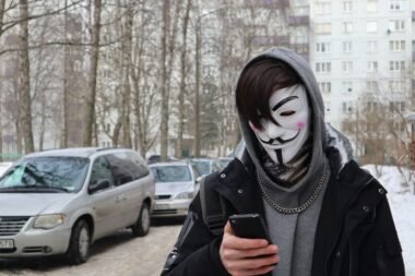 Eine Person mit Maske hält ein Smartphone in der Hand, Fokus auf die digitale Kommunikation im öffentlichen Raum.