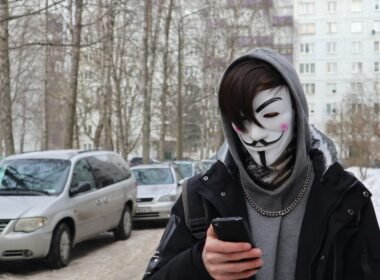 Eine Person mit Maske hält ein Smartphone in der Hand, Fokus auf die digitale Kommunikation im öffentlichen Raum.