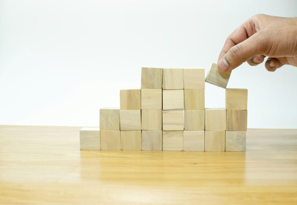 Eine Person platziert sorgfältig einen Holzblock auf einen Stapel aus mehreren Holzblöcken als Metapher für Unternehmensaufbau.